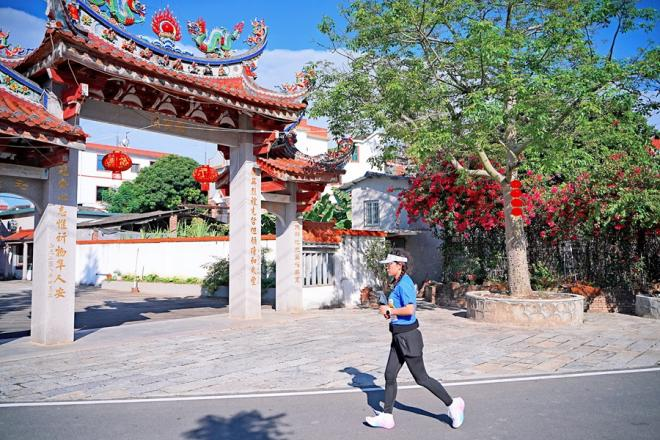 在特色建筑映襯下，一名選手在村道上奔跑。漳州市龍文區(qū)融媒體中心供圖